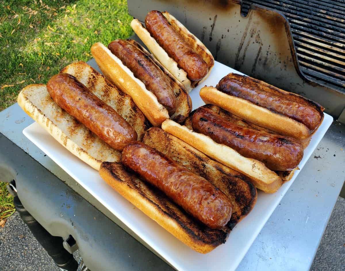 Grilled bratwurst in buns next to a grill