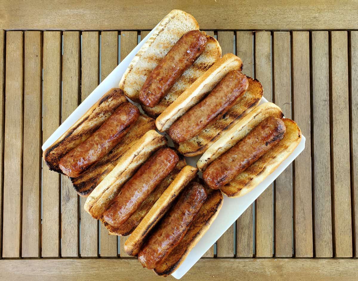 Six grilled bratwurst on buns on a plate on a wooden table