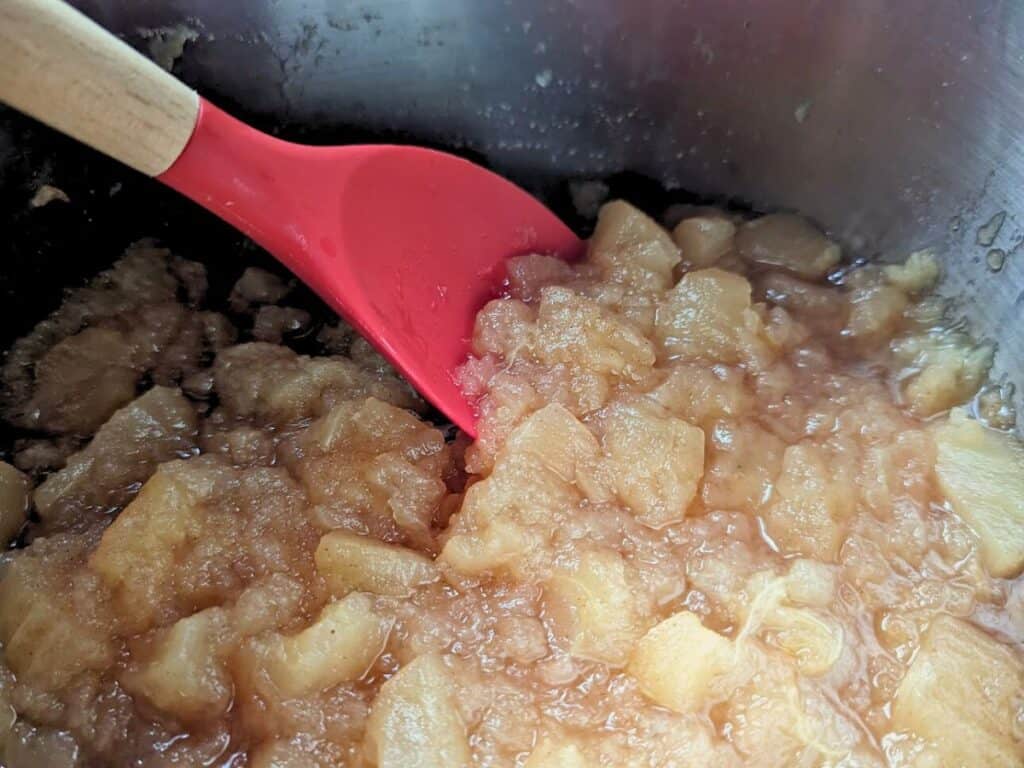 Image shows stirring cooked applesauce.