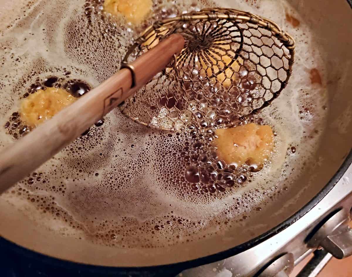 Using a spider tool to flip pumpkin donut holes cooking in oil.