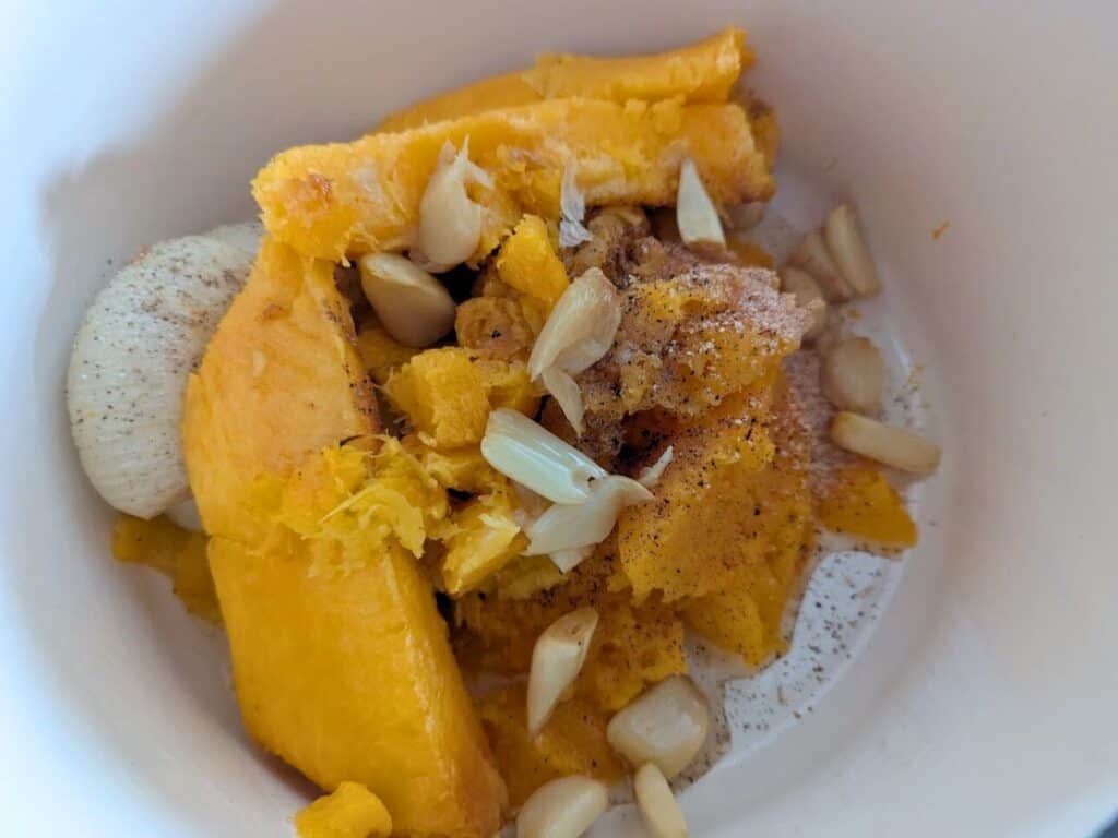 Image shows flesh of butternut soup with the garlic and onion in a pot.