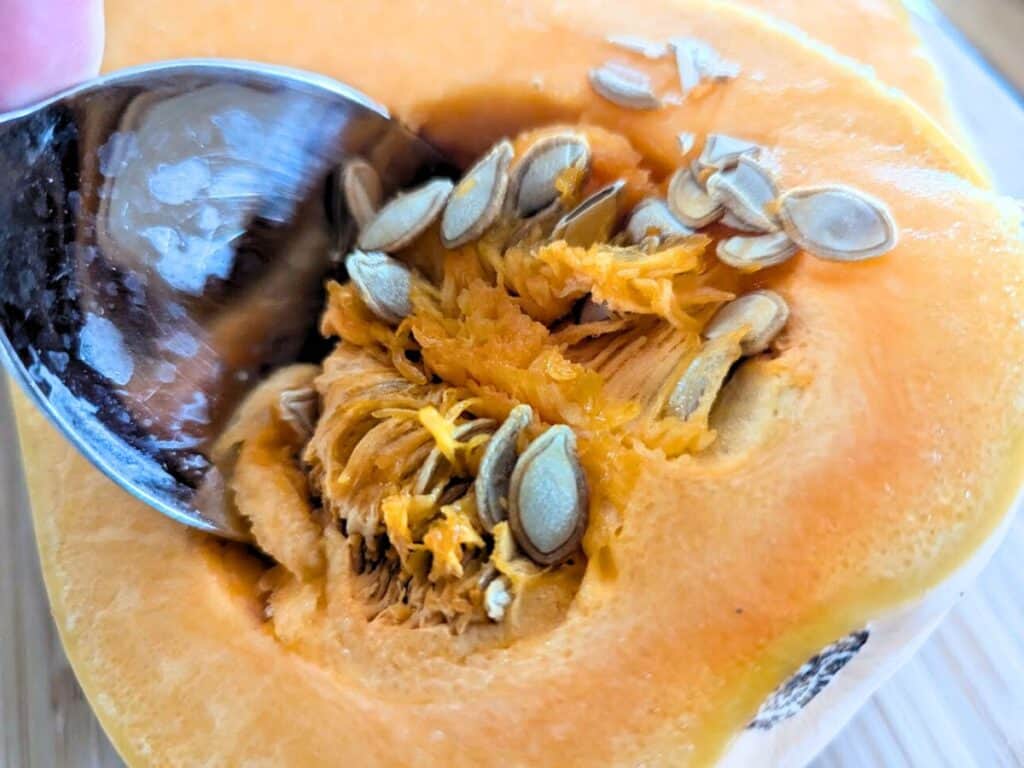 Image shows getting seed out of butternut squash using a spoon.
