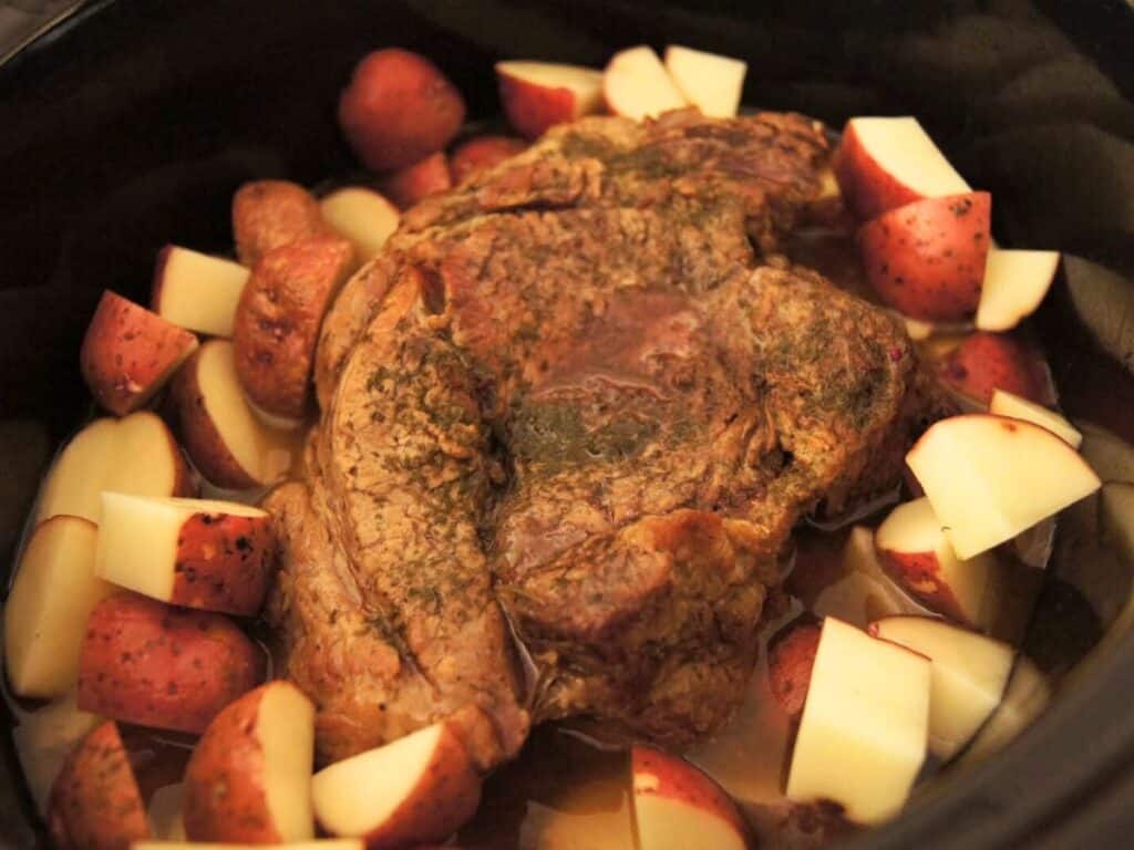 Image shows red potatoes added to the ingredients of pot roast in the crock pot.