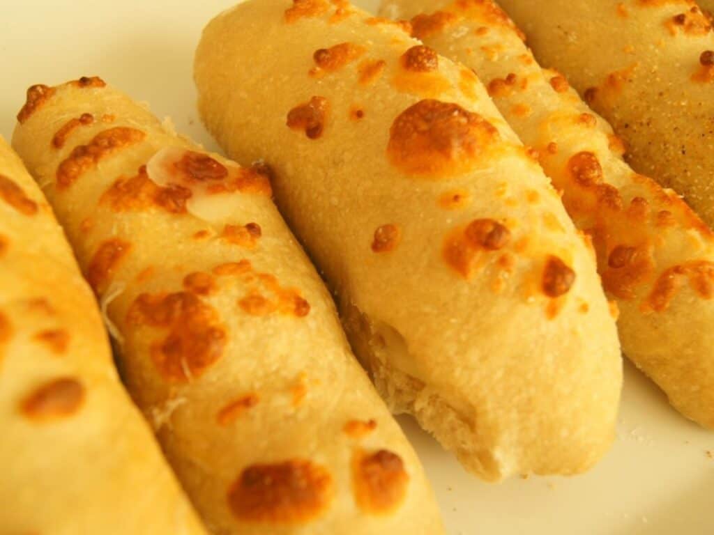 Image shows cheesy breadsticks on a white platter.