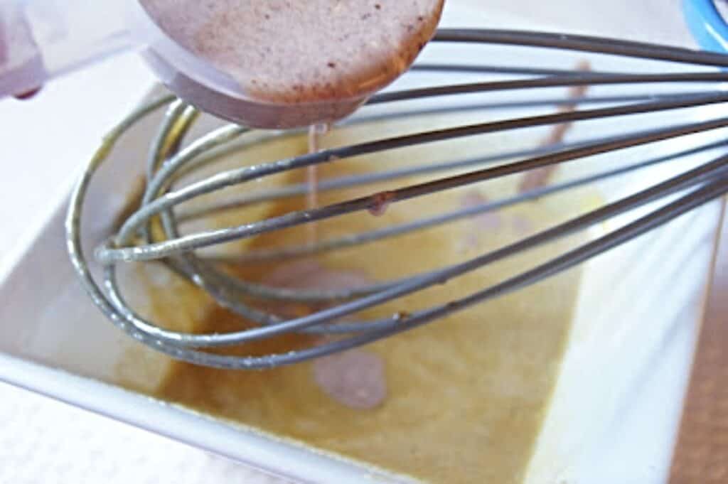 Adding chocolate cream to beaten egg yolks in a white bowl with whisk.