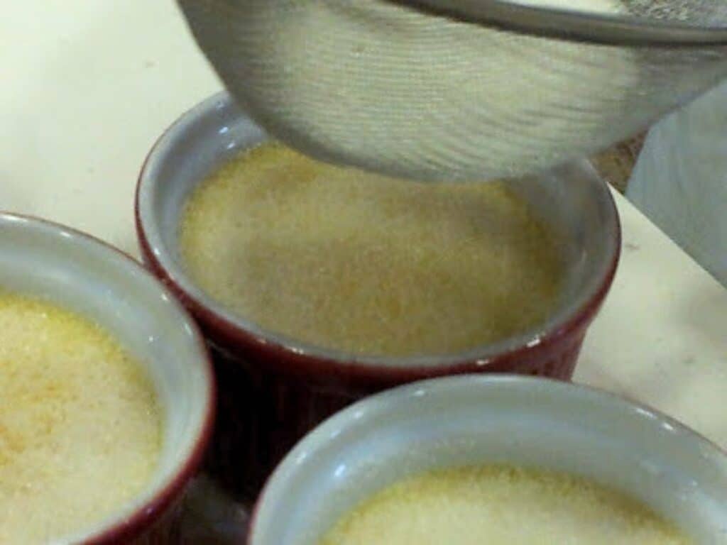 Image shows creme brulee coated with sugar before torching.