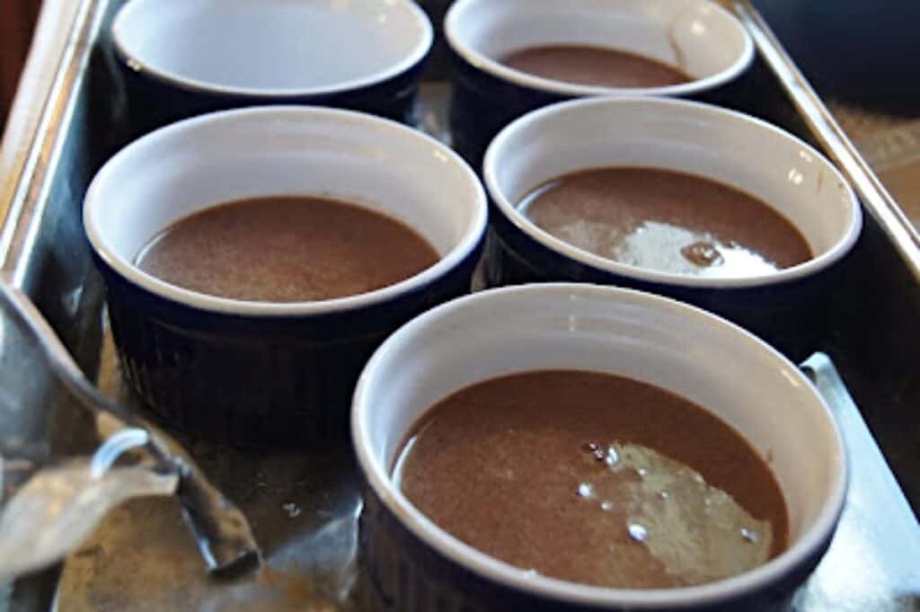 Filling water bath for ramekins with chocolate pots de creme with a liquid measuring cup.