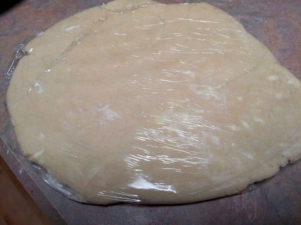 Image shows pie dough covered with plastic wrap.