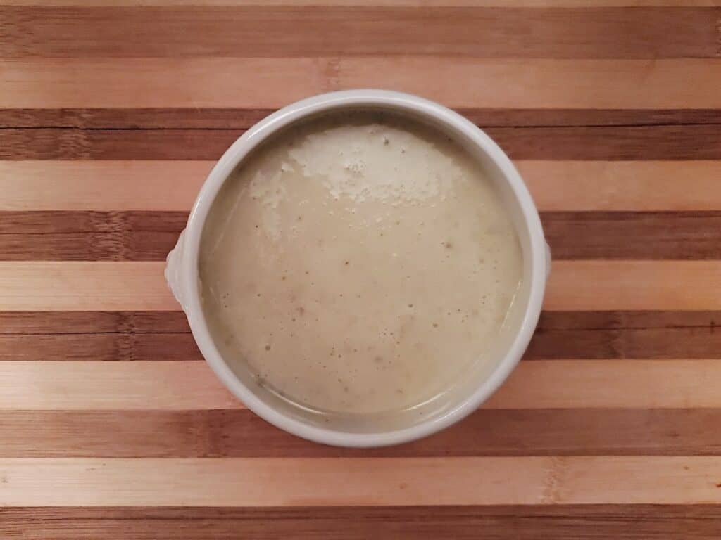 Overhead view of a bowl of homemade cream of celery soup on a wooden board.