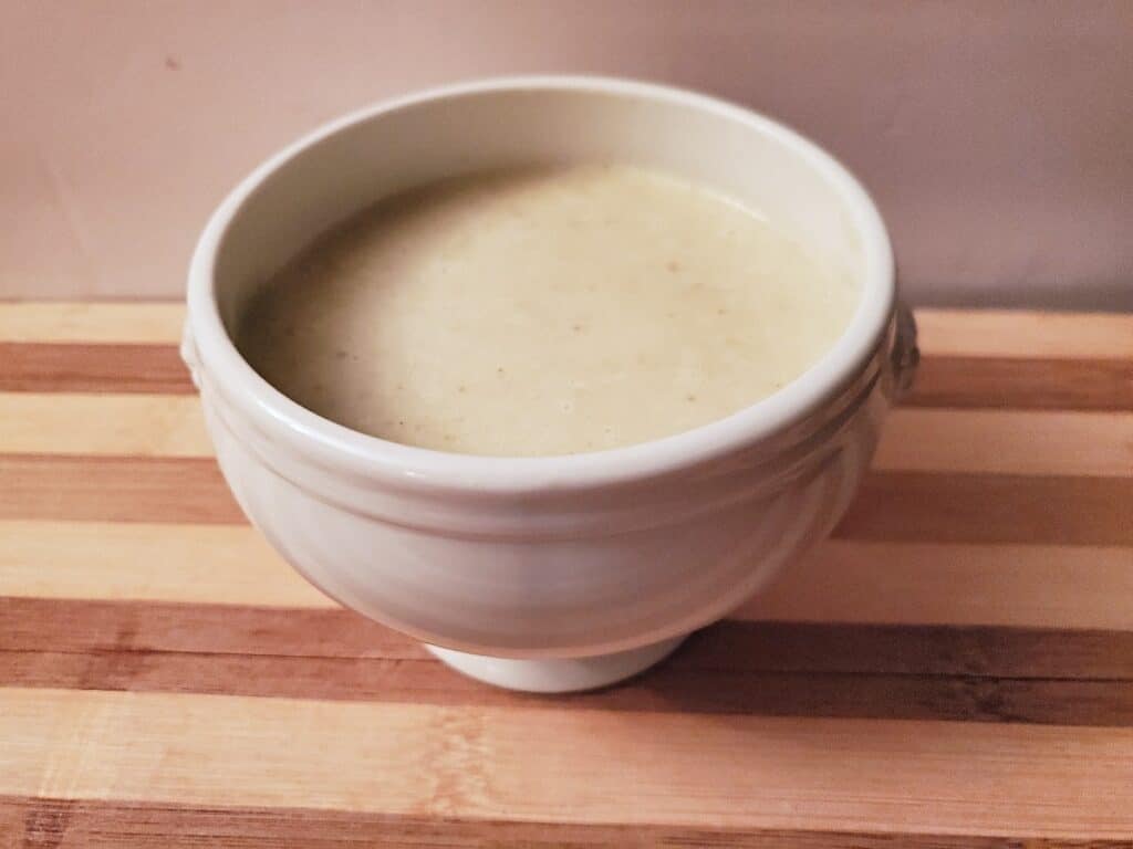 White bowl of homemade cream of celery soup on a wooden table.