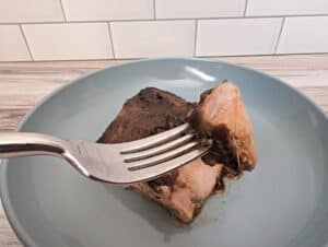 Fork holding a bite of asian marinated salmon with the rest of the fillet on a blue plate in the background.
