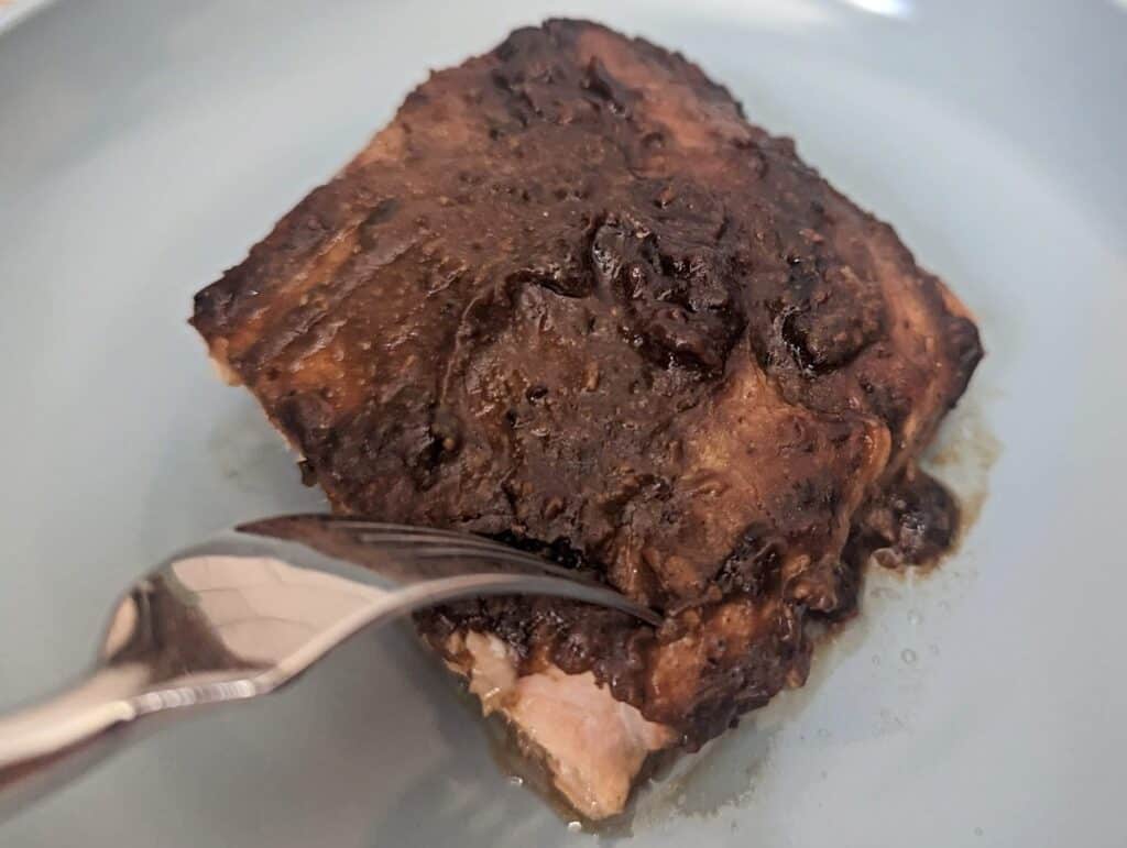 Overhead of a fork cutting into a glazed salmon fillet on a blue plate.