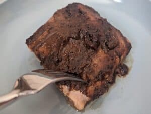 Overhead of a fork cutting into a glazed salmon fillet on a blue plate.