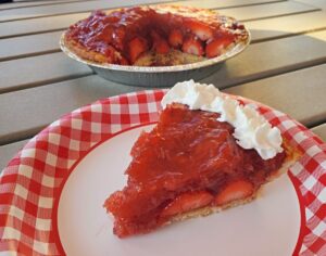 Close up of fresh strawberry pie slice with the remaining pie in the background.