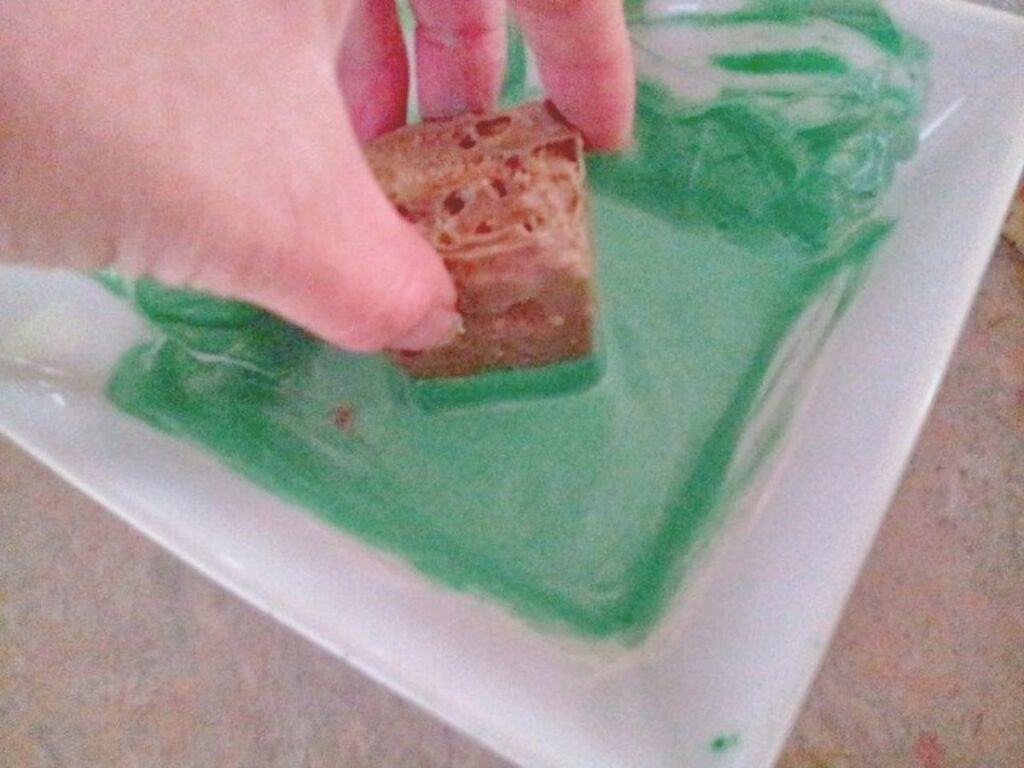 Image shows dipping the top of the cake squares in the green chocolate.