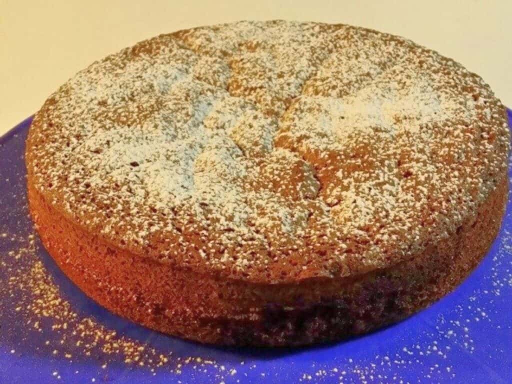 Image shows baked chocolate olive oil cake dusted with powdered sugar.