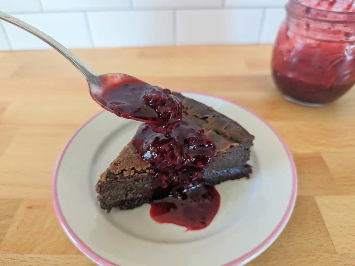 Image shows chocolate olive oil cake topped with jam on a plate.