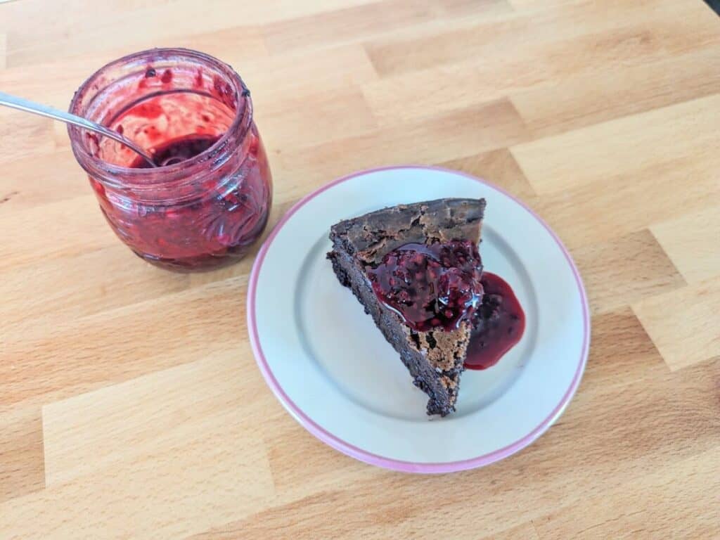 Image shows delicious chocolate olive oil cake topped with jam on a plate.