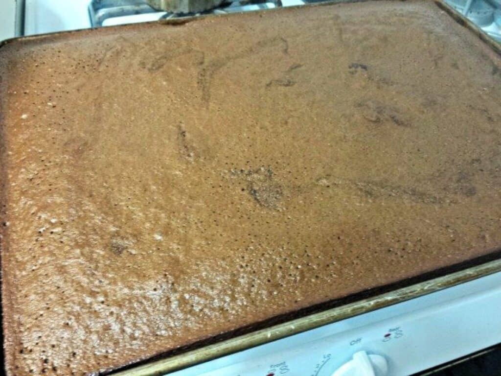 A large, freshly baked pan of Mexican sheetcake brownies sits on a stovetop, rich with chocolatey goodness and ready to serve.