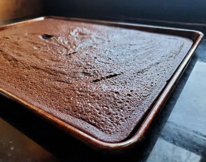 Baked sheetcake brownie not yet frosted sitting on a black countertop.