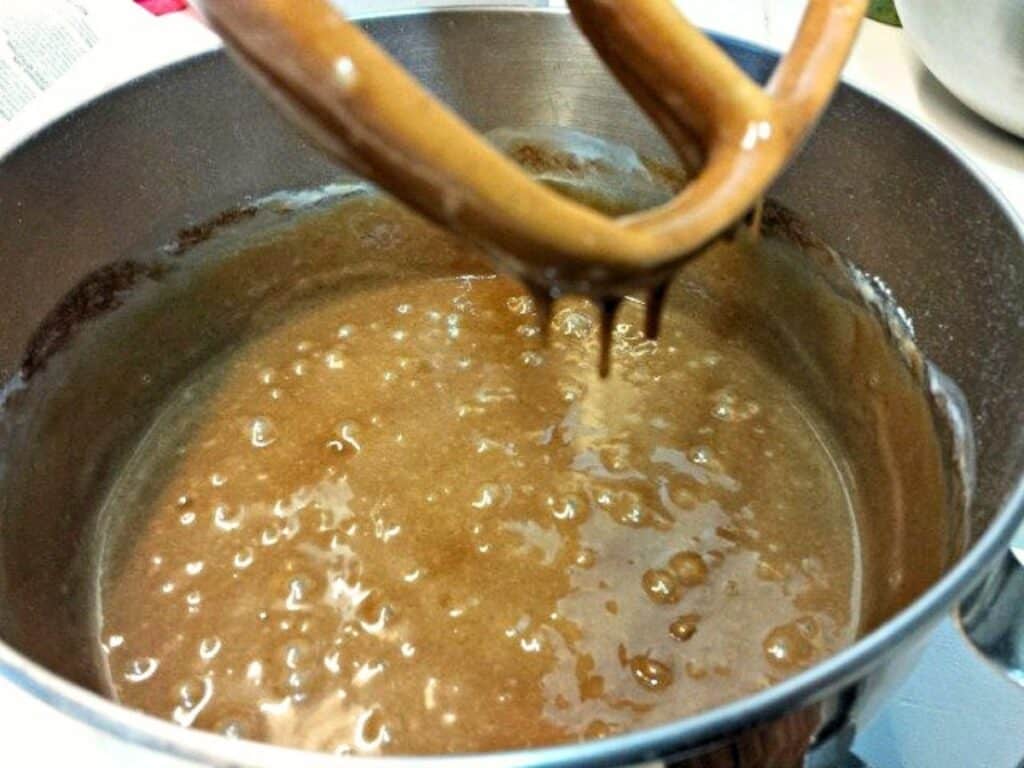A mixing bowl filled with brown cake batter for Mexican sheetcake brownies, with a stand mixer paddle attachment partially visible and coated in batter.