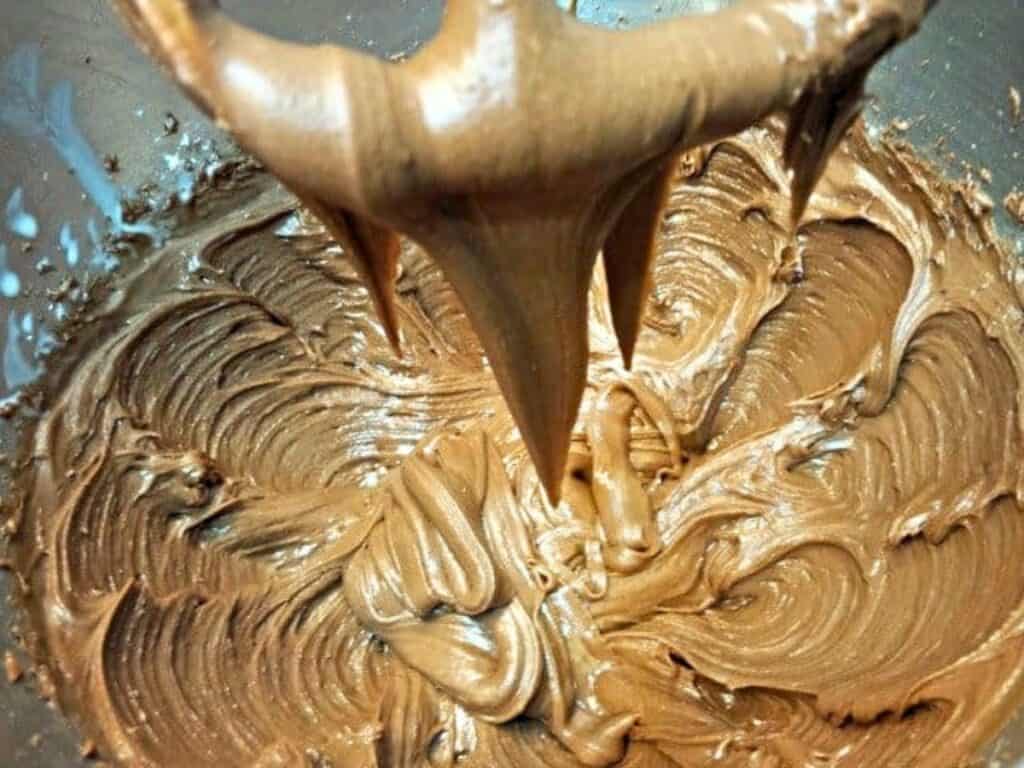 Chocolate cake batter being mixed in a metal bowl, with some batter clinging to the metal mixer attachment above—reminiscent of the rich, velvety texture found in classic Mexican sheetcake brownies.