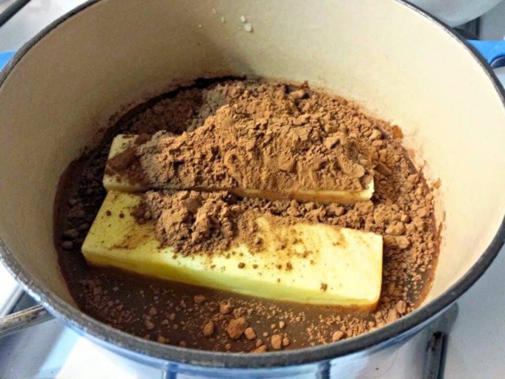 Two sticks of butter and cocoa powder in a pot, partially melted, on a stove, being prepared for cooking the rich base of Mexican sheetcake brownies.