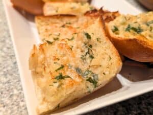 Slices of garlic bread with chopped parsley and melted butter on a white plate.