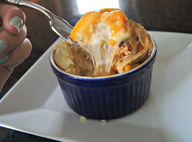 Image shows a fork with a great cheese pull taking a bite from a blue ramekin containing a chicken pizza pot pie.
