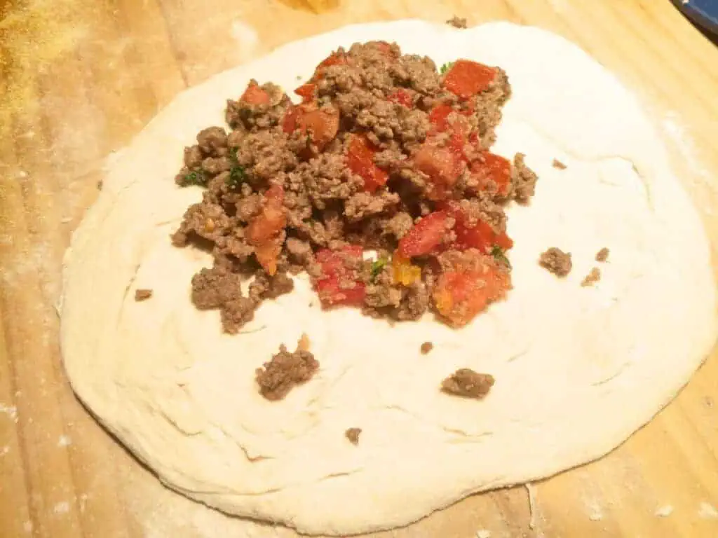 Image shows placing meat filling on dough.