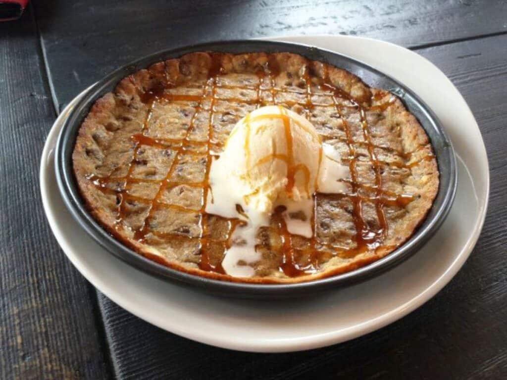 Image shows Deep dish chocolate cookie with a scoop of vanilla ice cream and caramel drizzle on top.