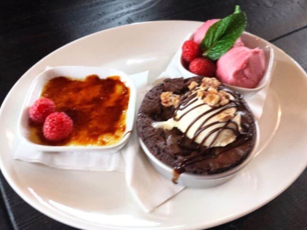 Image shows vanilla creme brulee, brownie with vanilla ice cream and raspberry sorbet on a single plate.