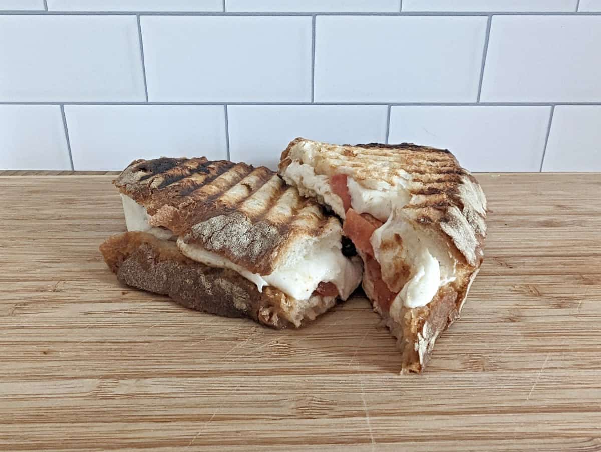 Image shows a sliced caprese panini on a wooden board with the melted cheese oozing out.