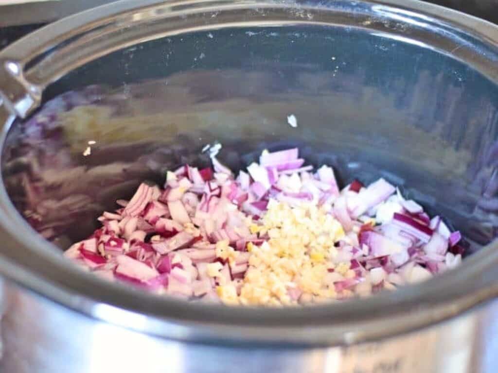 Diced red onions and minced garlic in a slow cooker, ready for cooking flavorful crockpot Mexican beef.
