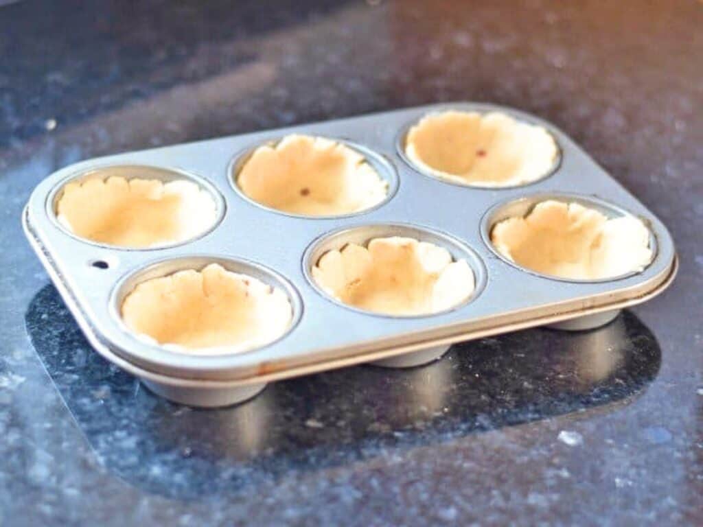 A six-cup muffin tin filled with unbaked pastry dough sits on a dark countertop, ready for baking—perfect for serving alongside hearty dishes like crockpot Mexican beef.