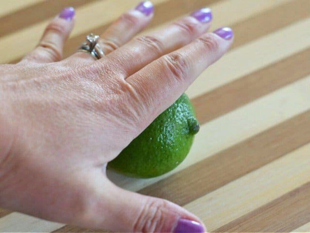 A hand with purple nail polish and a ring presses a lime on a striped wooden surface, ready to add fresh zest to tender crockpot Mexican beef.