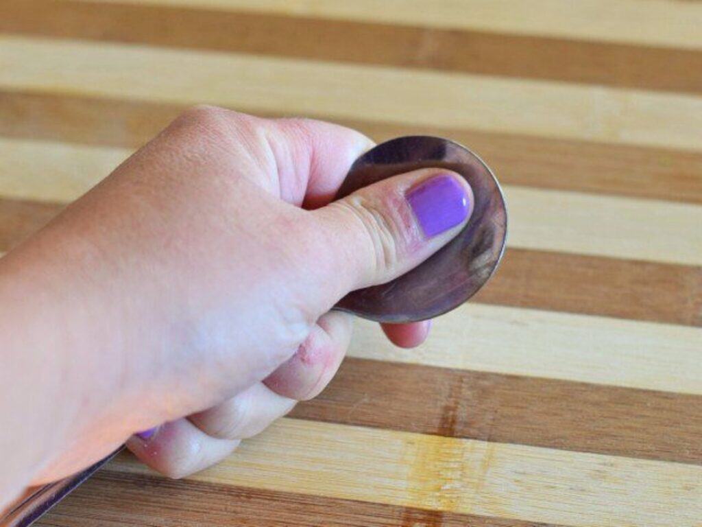 A hand with purple nail polish holds a pizza cutter over a striped wooden cutting board, ready to slice into some delicious crockpot Mexican beef flatbread.