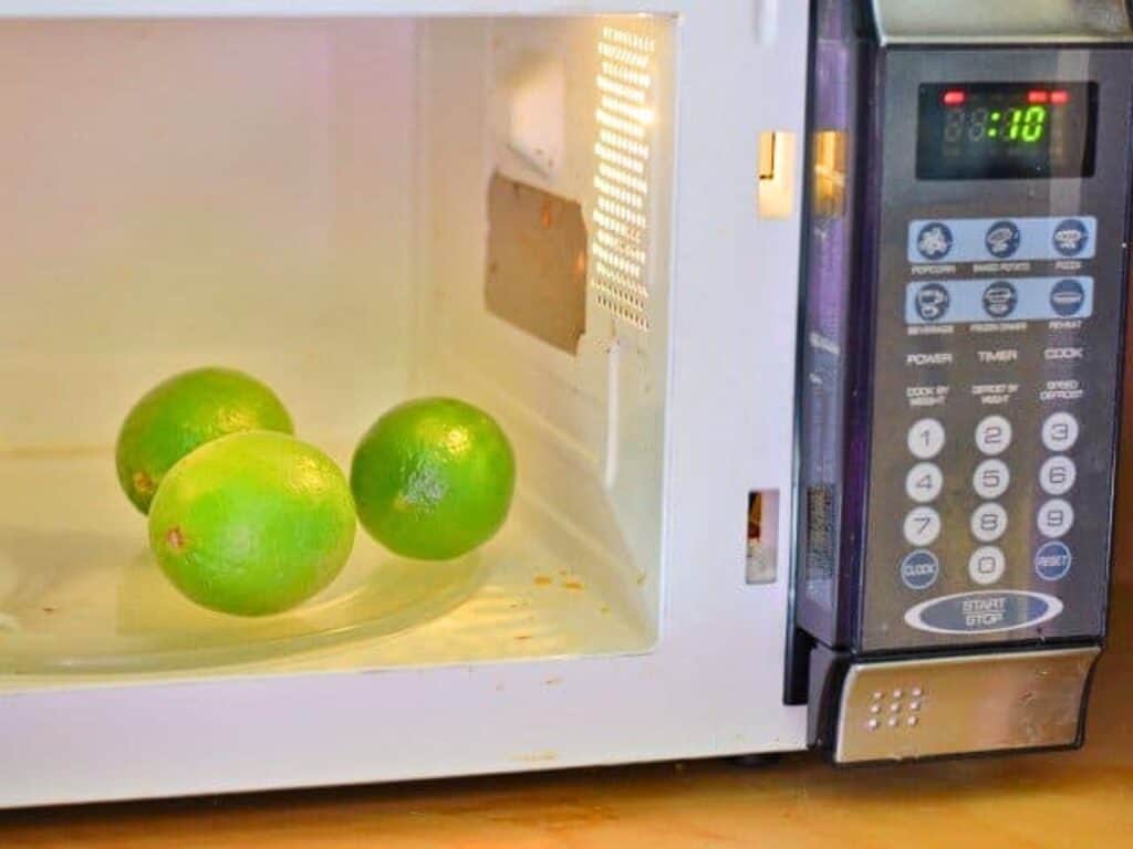 Three whole limes sit inside a microwave oven, which is turned on for one minute and ten seconds, as shown on the digital timer display—perhaps ready to be juiced for a flavorful crockpot Mexican beef recipe.