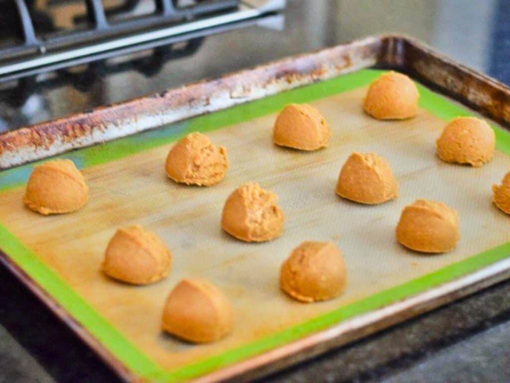 Twelve scoops of s&rsquo;mores cookie dough are evenly spaced on a baking sheet lined with a silicone mat, ready to be baked.
