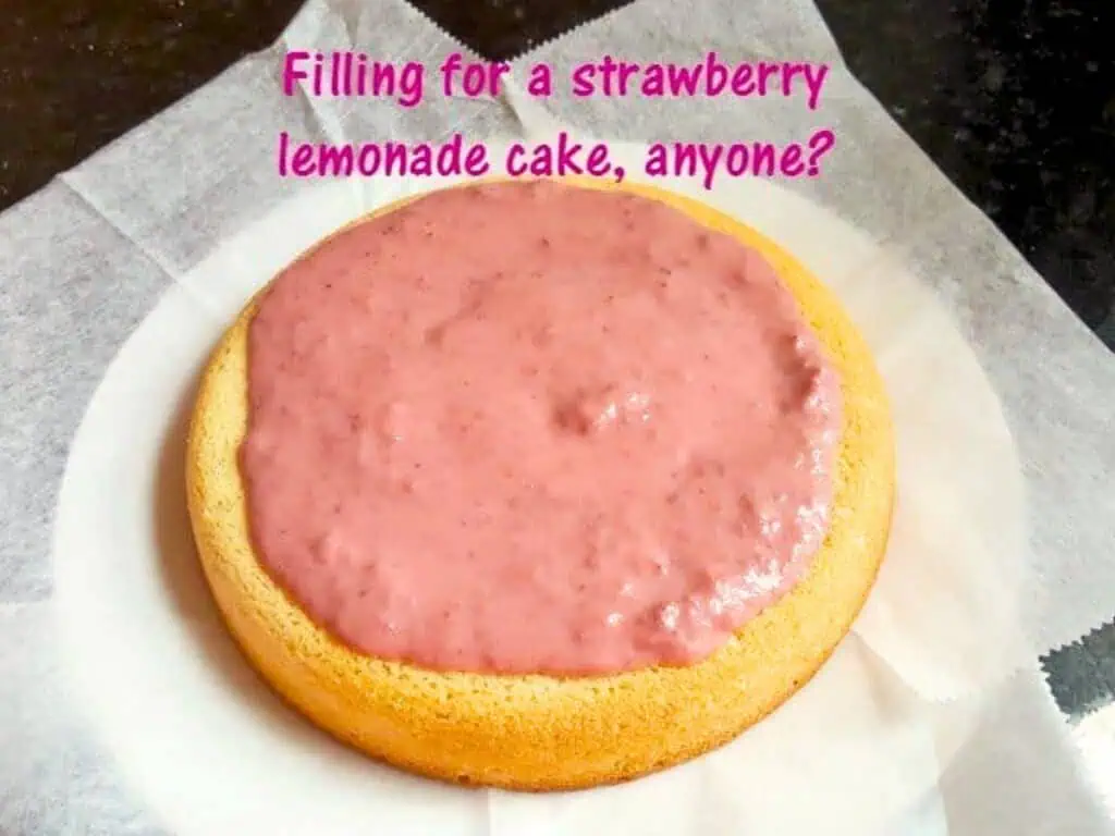 A round yellow cake layer topped with pink strawberry lemonade filling sits on parchment paper. Text above asks, "Filling for a strawberry lemonade cake, anyone?" For an extra burst of flavor, try adding luscious strawberry curd to the filling.
