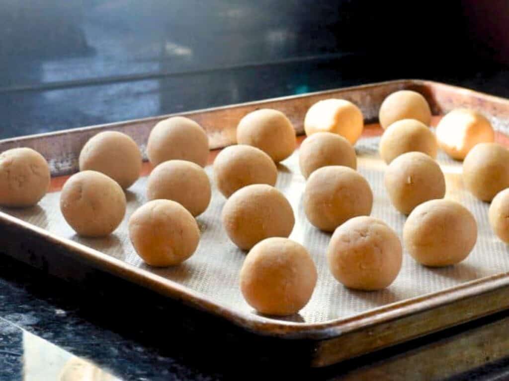 A baking tray with evenly spaced, round brown sugar cookie dough truffles placed on a silicone mat, ready to be baked.