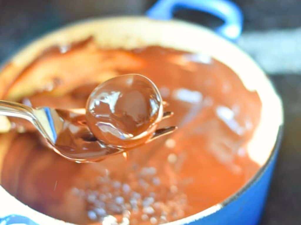 A fork holds a round brown sugar cookie dough truffle coated in melted chocolate above a blue pot filled with more melted chocolate.