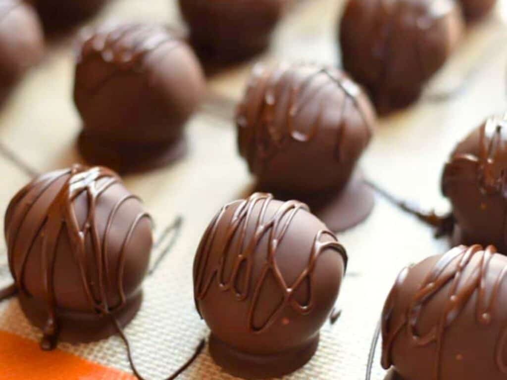 Rows of round brown sugar cookie dough truffles with a dark chocolate drizzle, arranged on a textured surface.