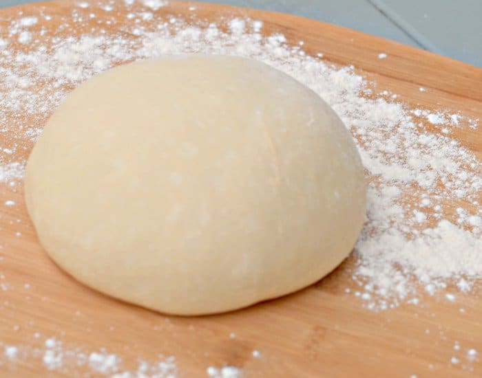 Round of pizza dough sitting on a wooden board.