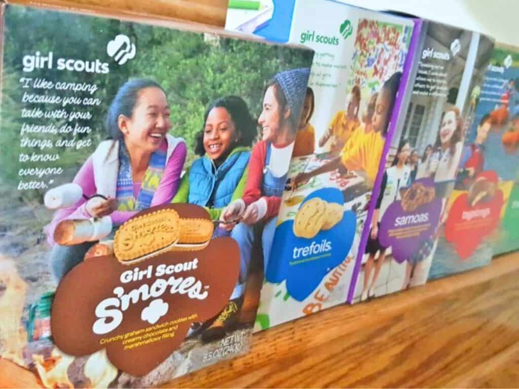 Image shows Girl Scout cookie boxes piled on a wooden platform.