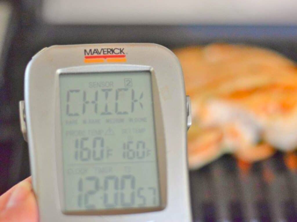 A digital meat thermometer displays 160&deg;F for chicken, with grilled kung pao chicken salad visible in the blurred background.