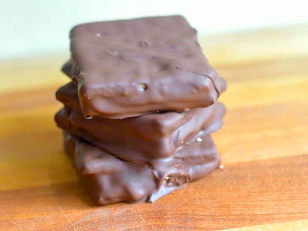 Four chocolate-covered s'mores cookies are stacked on a wooden surface.