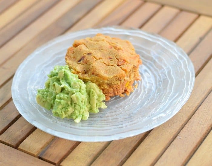 Image shows a Tamale pot pie on a glass plate with guacamole sitting next to it.