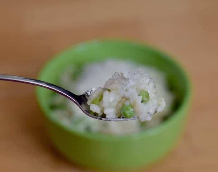 Image shows a Spoonful of risotto with peas and lemon with the rest of the bowl in the background.