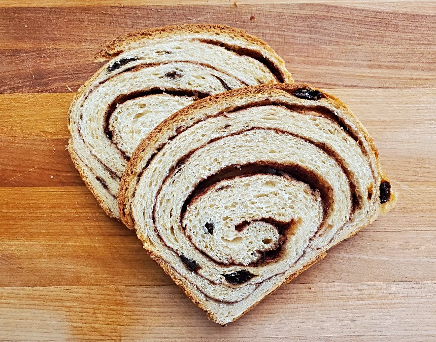 Image shows an overhead view of Cinnamon Raisin Bread with part of the loaf sliced.